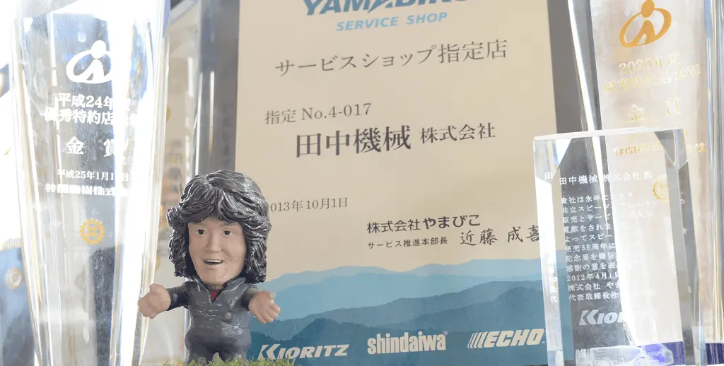 YAMABICOサービスショップ指定店の認定証と複数のトロフィーが飾られ、田中機械株式会社の指定No.4-017が記載された表彰コーナー