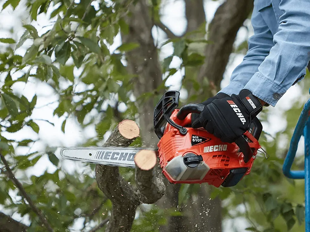 チェーンソーで樹木を切断中、木屑が舞い散る実際の使用風景、オレンジと黒のボディで屋外作業の様子