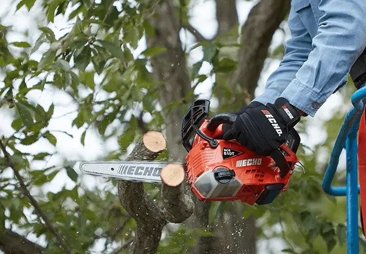 チェーンソーで樹木を切断中、木屑が舞い散る実際の使用風景、オレンジと黒のボディで屋外作業の様子