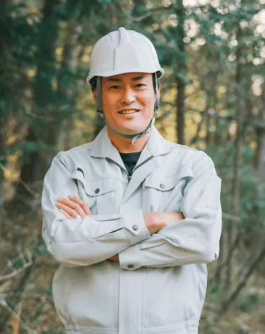 腕を組んで自信に満ちた表情の建設作業員、白いヘルメットとグレーの作業服を着用